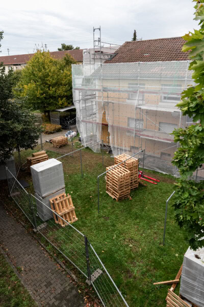 Bauarbeiten an einem Gebäude mit Gerüst und Bauholz im Garten.